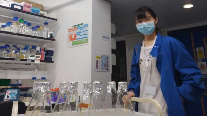 Julia Soh wearing a mask, standing over a table in the lab.