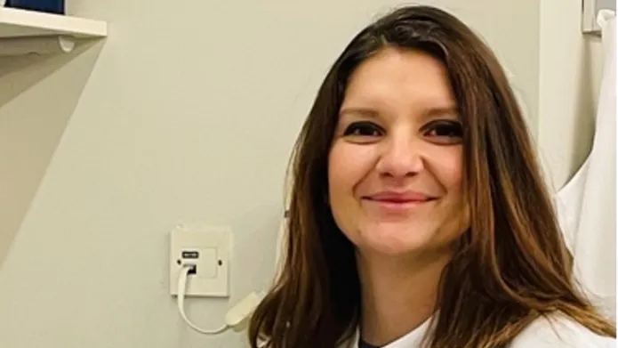 Ralitsa Madsen sitting at a desk in the lab, wearing a lab coat and blue gloves.