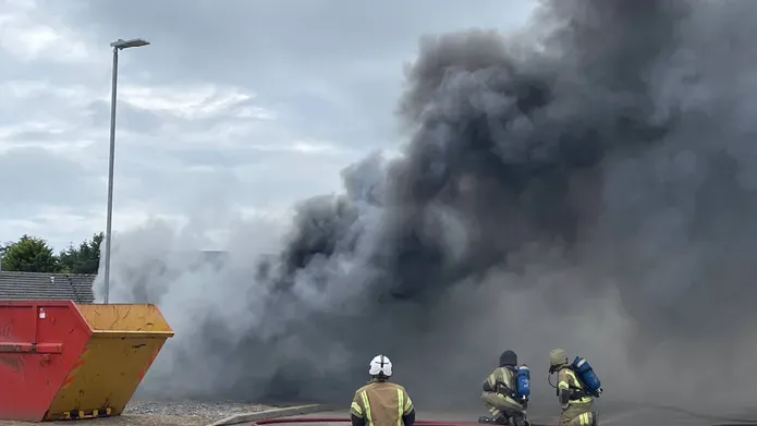 Three fire fighters sit with water houses outside a burning testing facility for training purposes