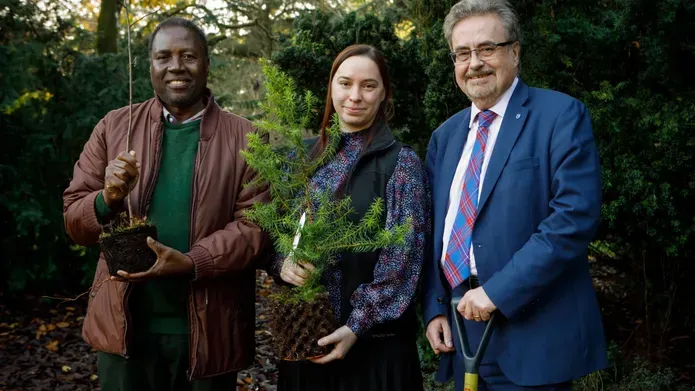 Principle stead with a spade and two other people holding small trees. 