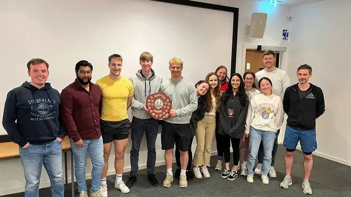 A group of students lined up in a row with one person holding a trophy