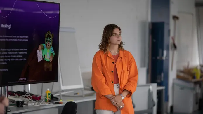 A student presenting at a design sprint for DJCAD with a tv monitor in the background