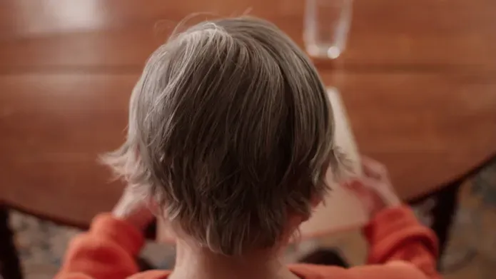 A close up of an elderly woman's head as she reads a book at a table