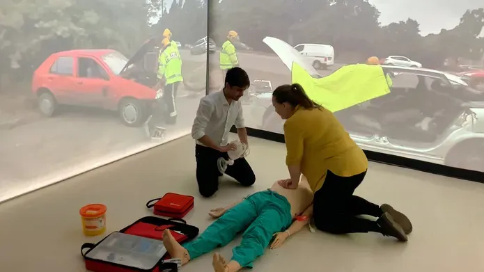 A demonstration of CPR in the Immersion Room, with car crash scene projected in the background