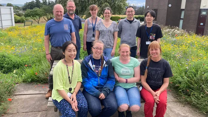 Paul Birch and his team sitting outside a building at a bench surrounded by wildflowers 