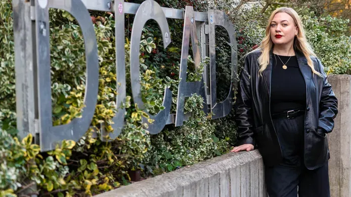 Wonan with blonde hair wearing black stood outside next to the DJCAD sign