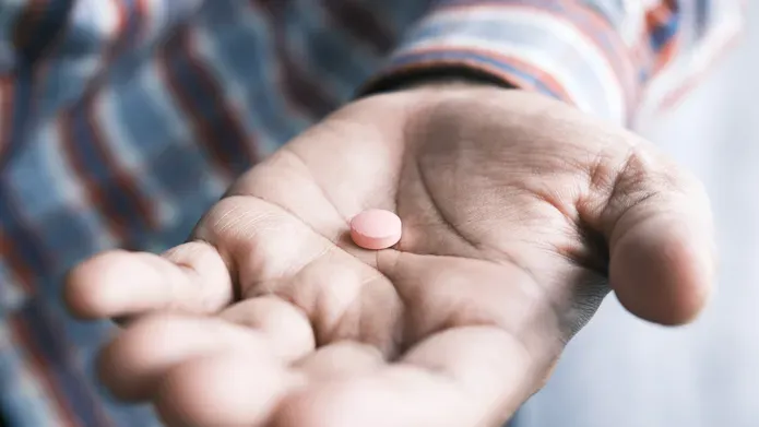 A man's hand outstretched with a pill in his palm