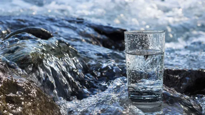A glass of water sitting on a rock in a river.