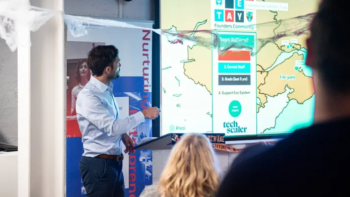 A man stands in front of a screen presenting to a room of people.