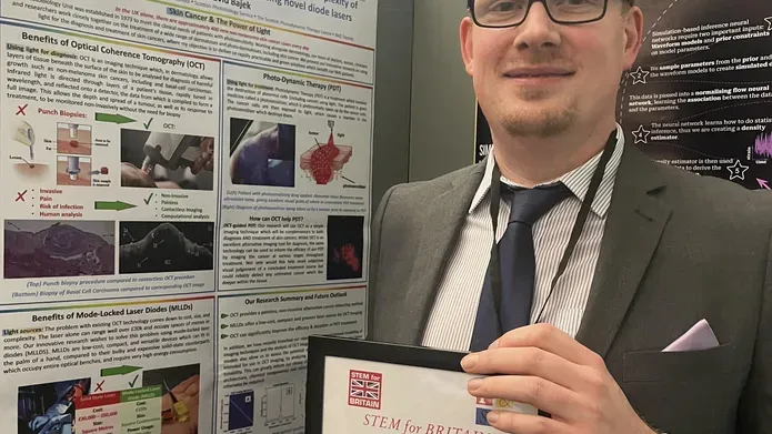 Man wearing suit, shirt and tie, standing next to an information poster, holding a certificate.