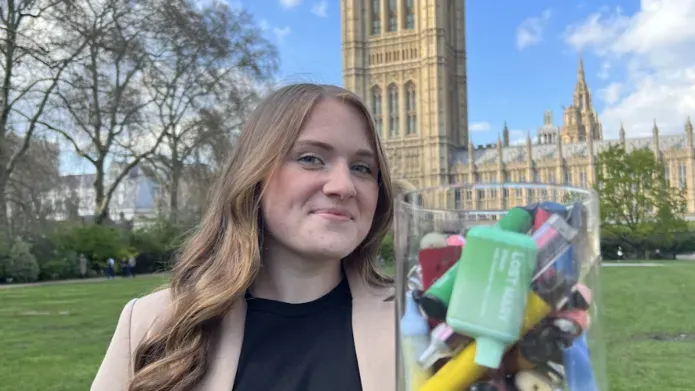 Woman holding a jar filled with discarded disposable vapes, standing outside Westminster