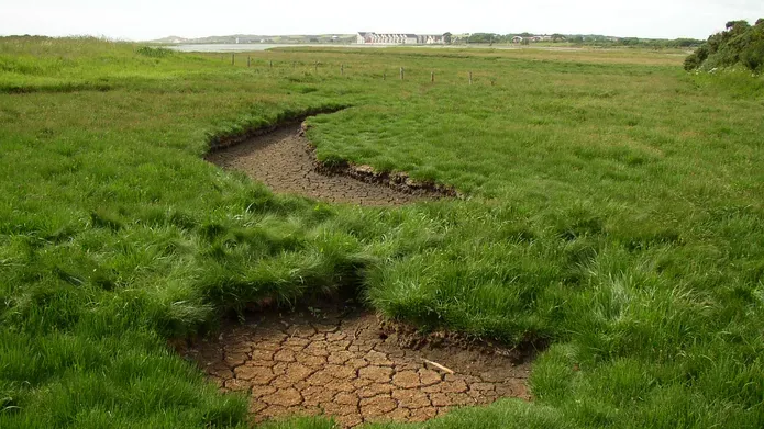 image of small stream which has run dry and dry soil has been exposed, running though a grassy hill