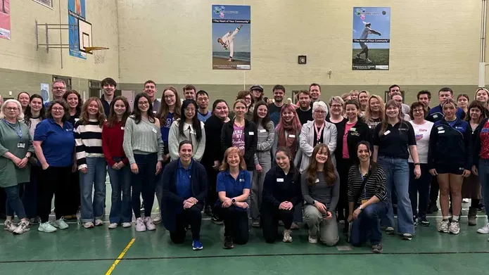 A group of people stand in a sports hall.