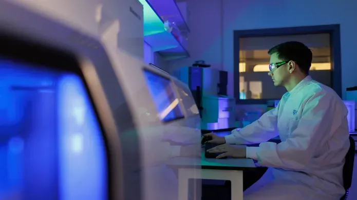 A man in a lab coat typing on a computer keyboard.