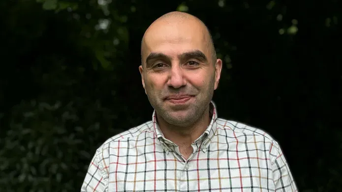 Profile shot of Professor Husam AlWaer. He is smiling and wearing a checkered shirt.