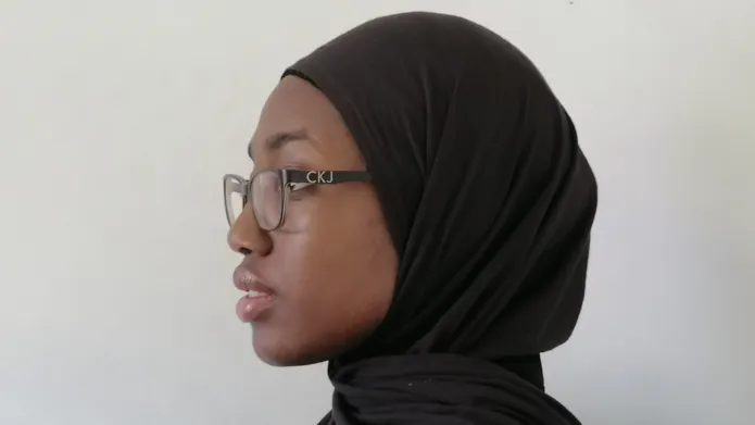 Side profile shot of Hanifah Sogbanmu, who wears a black hijab and glasses