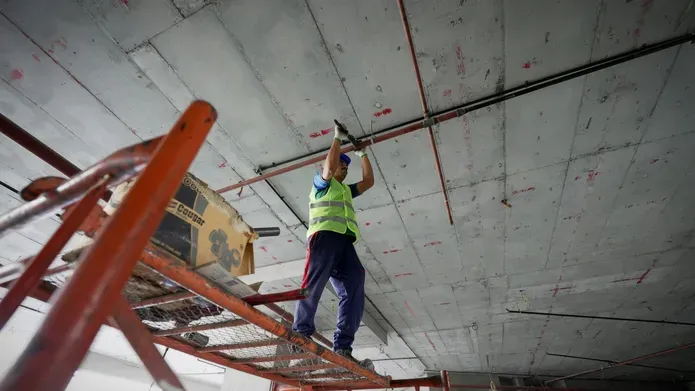 A construction worker on a cherry picker works on a concrete roof