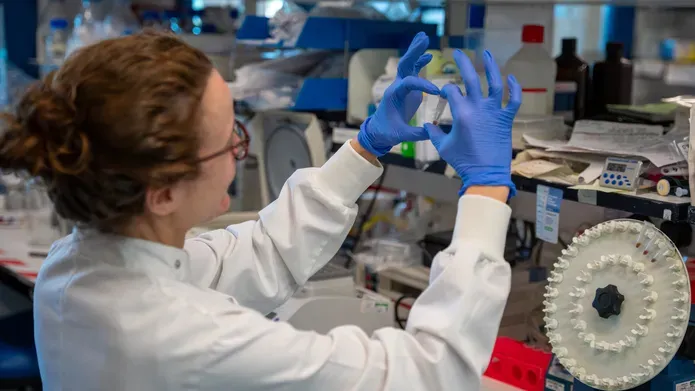 woman in lab wearing a lab coat and blue latex gloves holding up a vile