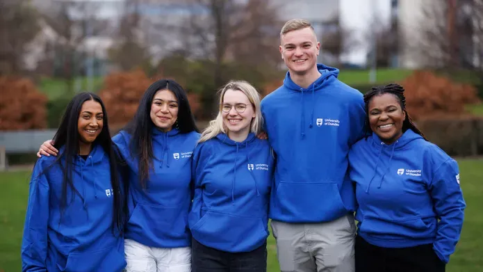 Five student sin blue uni jumpers stood together in a row smiling