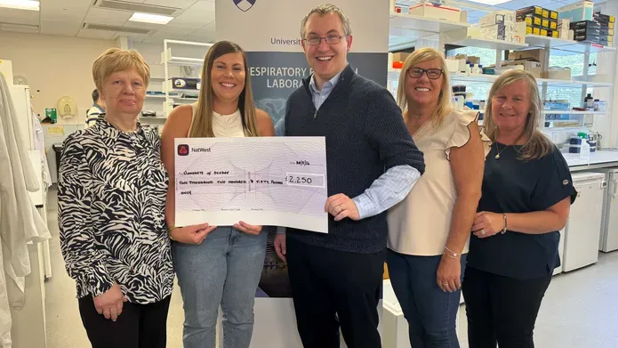 Five people stand together holding a large sized cheque.
