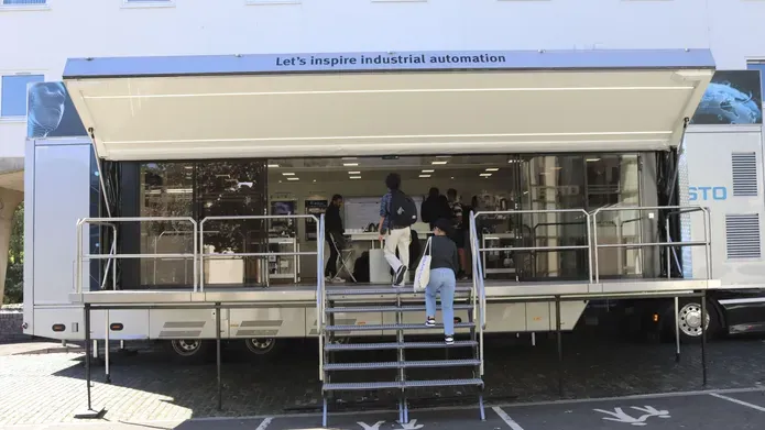An open sided trailer with people walking up the steps and entering. The words "Lets inspire industrial automation" are above the entrance.