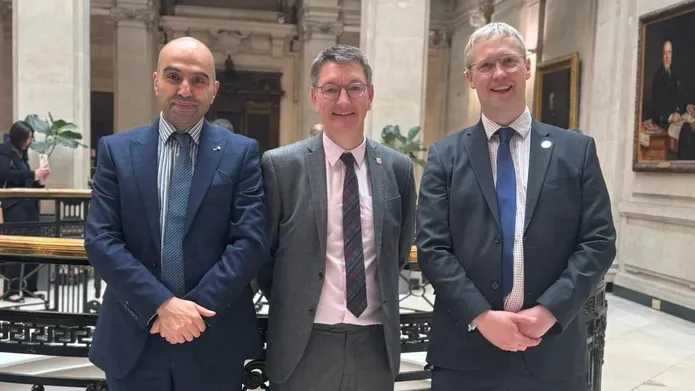 three men standing in a line wearing suits and ties and smiling at the camera