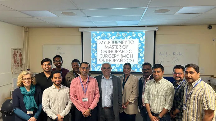 A group of people stand in front of a presentation screen, which says "My journey to master of orthopaedic surgery (MCH orthopaedics)