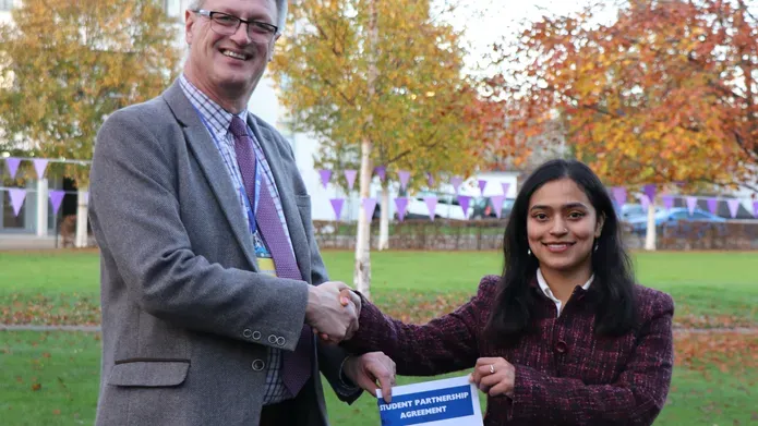 A man and woman shking hands holding a paper document
