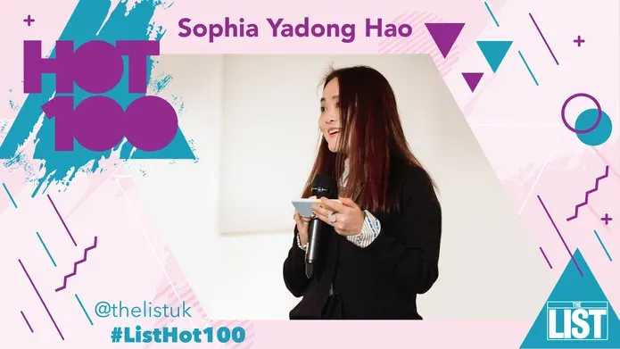 Woman in black blazer holding a microphone. Pink and blue graphics framing the image