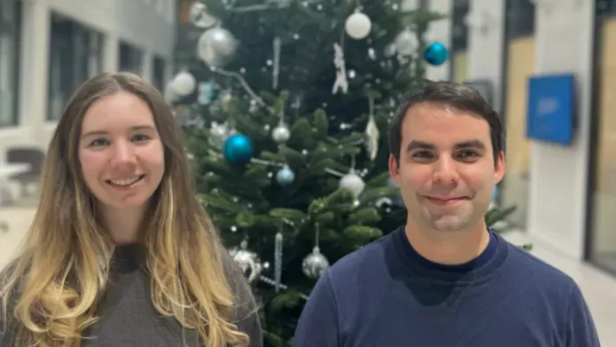 Two people smiling in front of a Christmas tree
