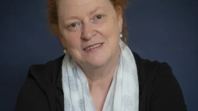 Woman with red hair wearing a light coloured scarf and dark top smiling with her arms folded