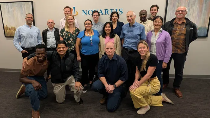 A group of people standing and kneeling together smiling in front of a sign saying Novartis