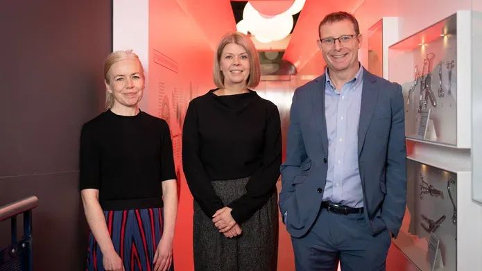 Dr Morag Martin, Dr Pamela Duke and Ronnie Palin standing, smiling, in an orange-lit corridor