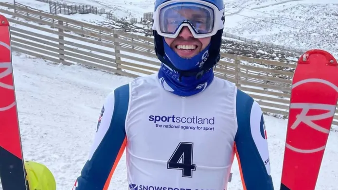A man wearing white and blue ski suit holding a ski in each hand.