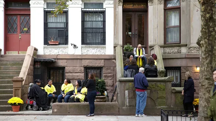 Performance photograph. Groups sit on the front steps of a new york street in discussion, performers wear yellow scarves
