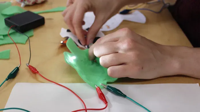 Two hands hold a piece of green material with electric wires clipped to it.