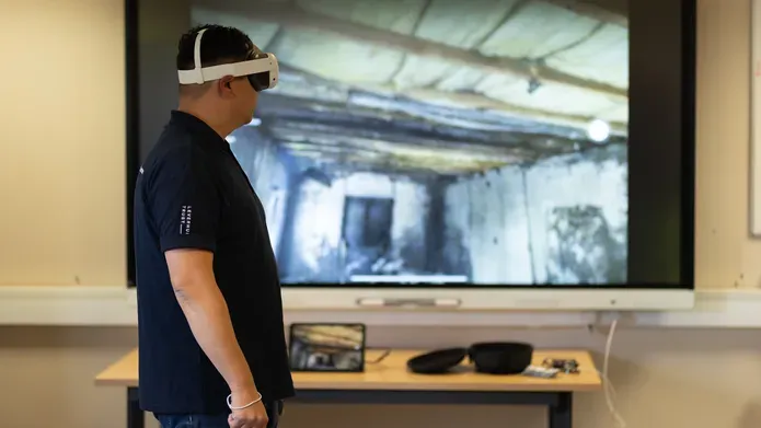 Man wearing a VR headset with a large screen behind him with showing a burnt out room