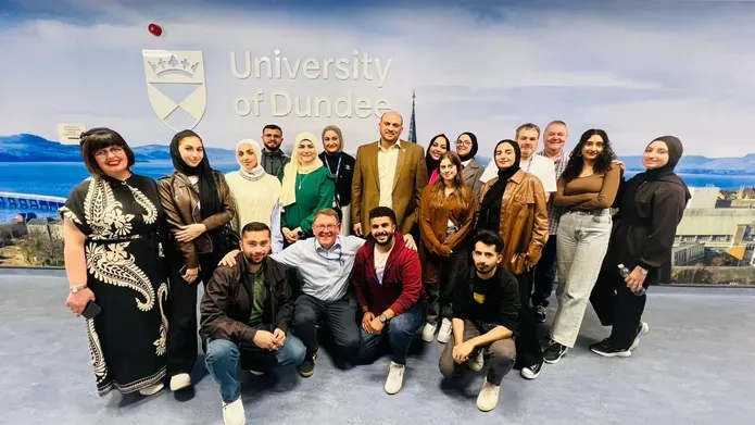 A group of students and a lecturer standing in front of a University of Dundee poster