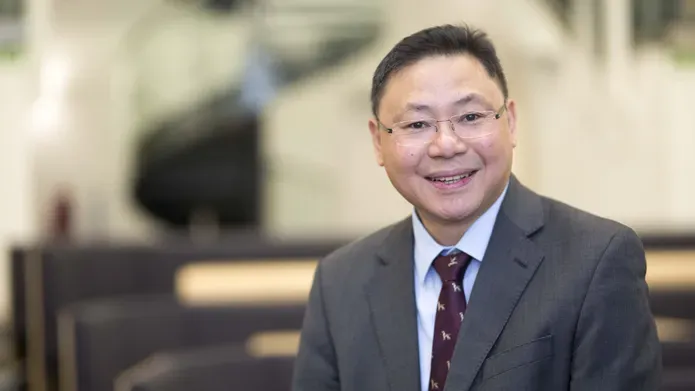 man wearing glasses and suit looking and smiling at camera. background is blurred
