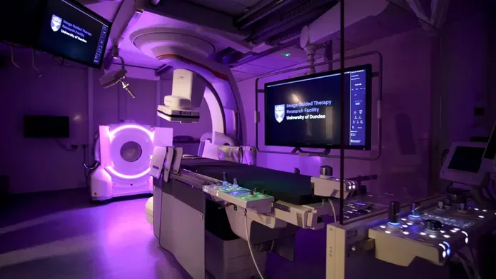  A room featuring a large screen mounted on the wall and medical imaging equipment in the foreground