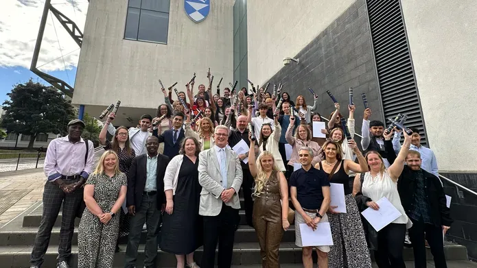 The University of Dundee's Access Summer School Class of 2024 stand on the steps of the University's Dalhousie Building, raising their certificates in the air in joy