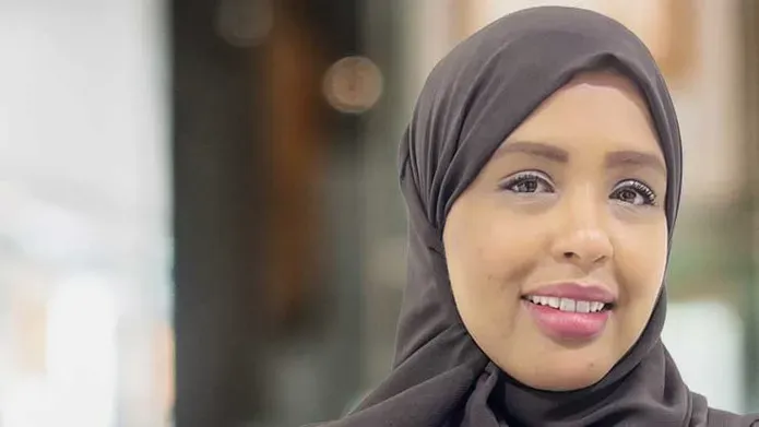 A person wearing a head scarf is looking forward, smiling.