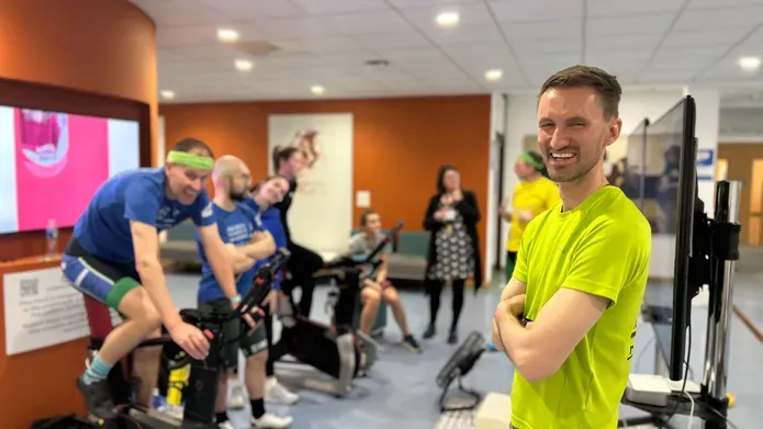 People on the left are using stationary bikes, a person stands to the left wearing a bright green t-shirt, laughing.