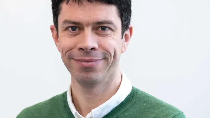 man with dark hair wearing a white shirt and green jumper