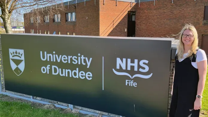 A woman standing in front of a large NHS and UoD sign outside