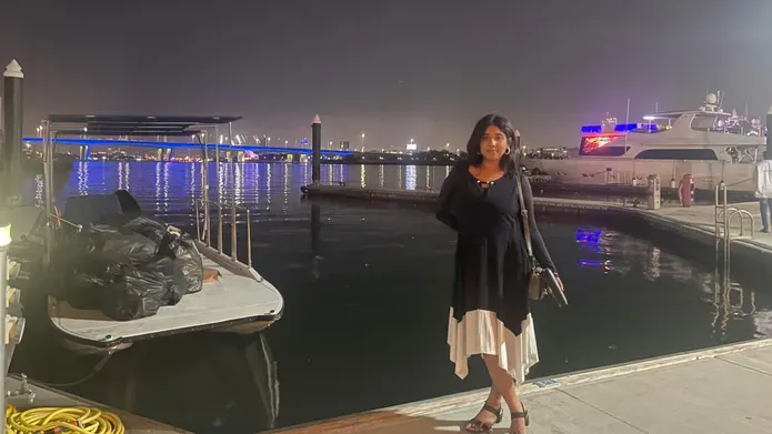 Sandra, standing at a harbour at night with yachts in the background