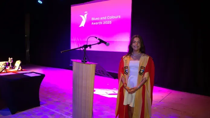 student in red and yellow robes stands on stage