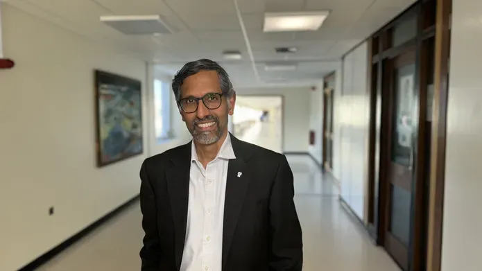 A person walks down a long white corridor, wearing a suit and smiling.
