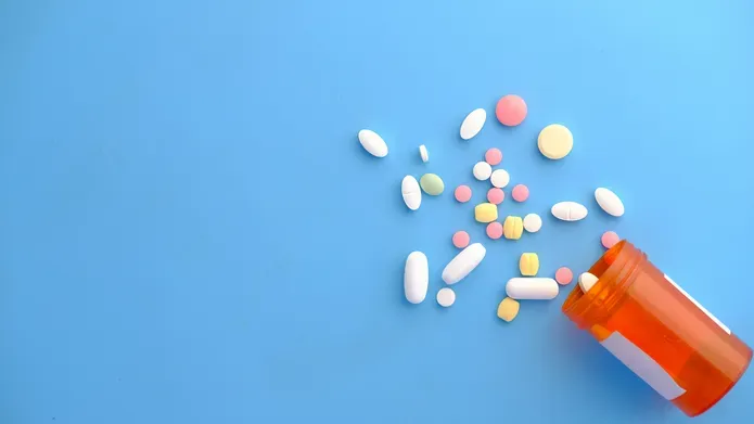 A blue background with a bottle of multicoloured pills spilled on to the surface