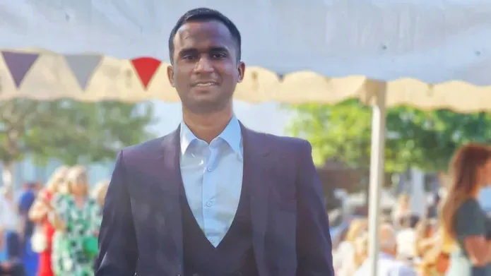 A person wearing a suit stands inside a white marquee with a red flag.